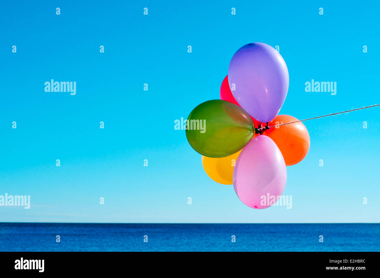 Un grappolo di palloncini di diversi colori volare nel cielo sopra l'oceano Foto Stock