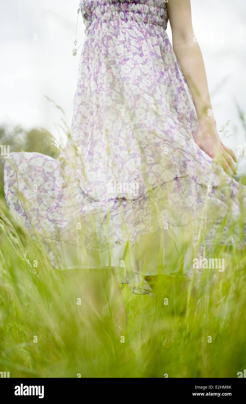 Donna in piedi nel campo erboso, abito soffiando nel vento, vista ritagliata Foto Stock