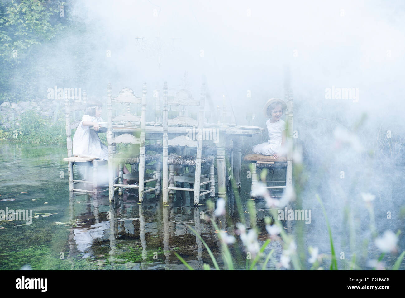 I bambini seduti al tavolo da pranzo galleggiante sul laghetto, circondati da fumo Foto Stock