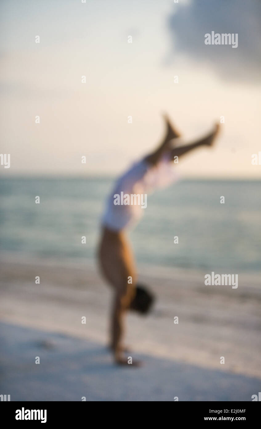 L'uomo facendo handstand sulla spiaggia al tramonto, sfocato Foto Stock