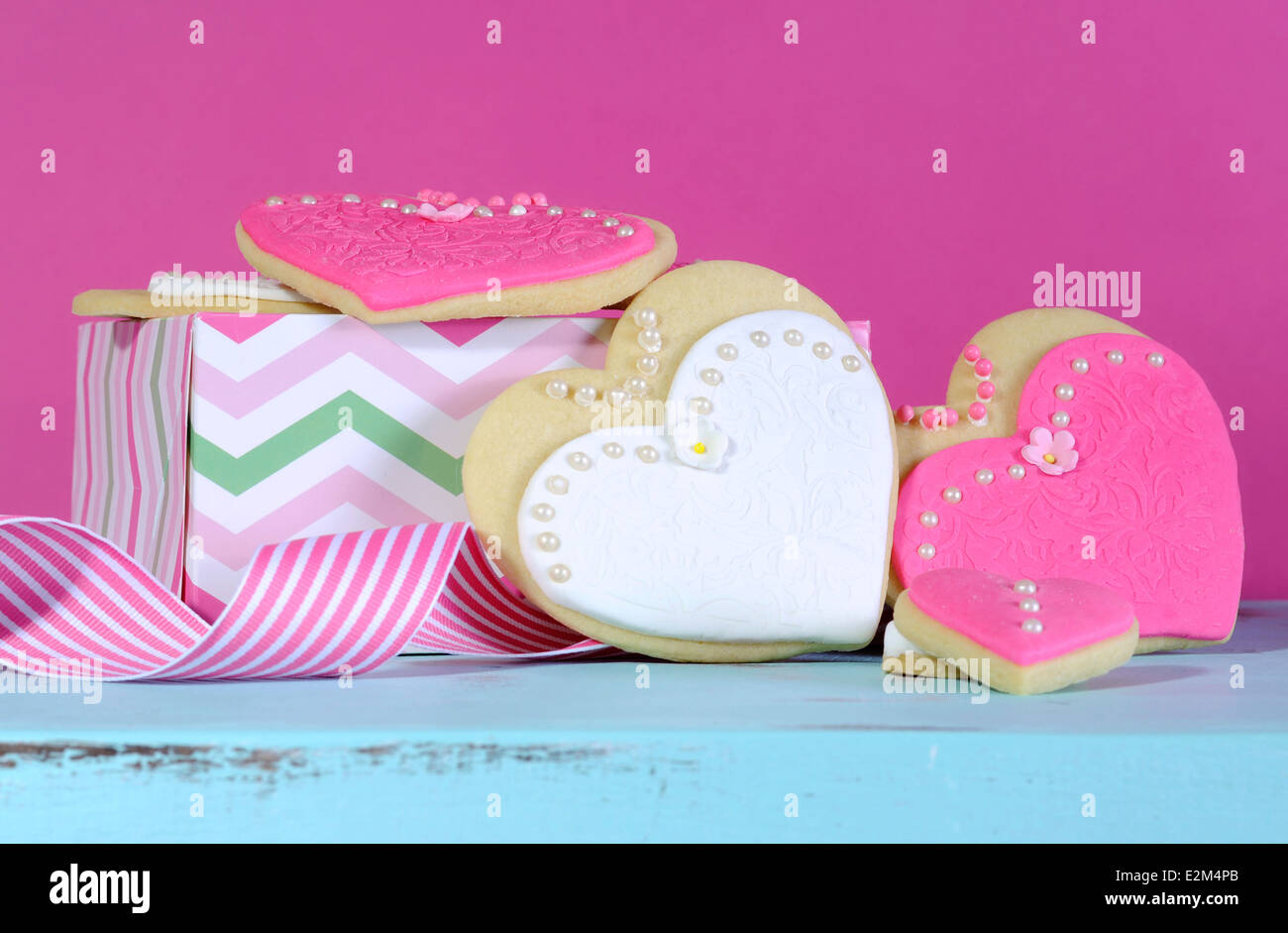 Rosa e Bianco sposa e le sue damigelle hanno wedding forma di cuore i cookie su vintage tavolo blu contro un luminoso rosa caldo dello sfondo. Foto Stock