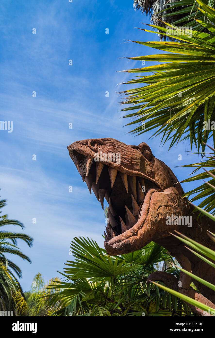 La testa arrugginita di un T Rex dinosaur scultura si distingue tra alberi di palma. Foto Stock