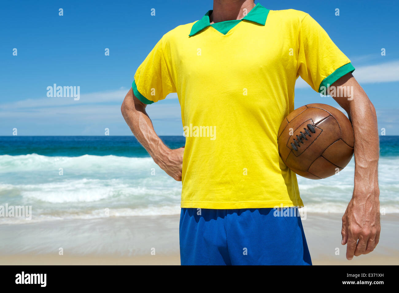 Il calcio brasiliano giocatore nel team Brazil colori tenendo il vecchio marrone vintage pallone da calcio sulla spiaggia tropicale Foto Stock