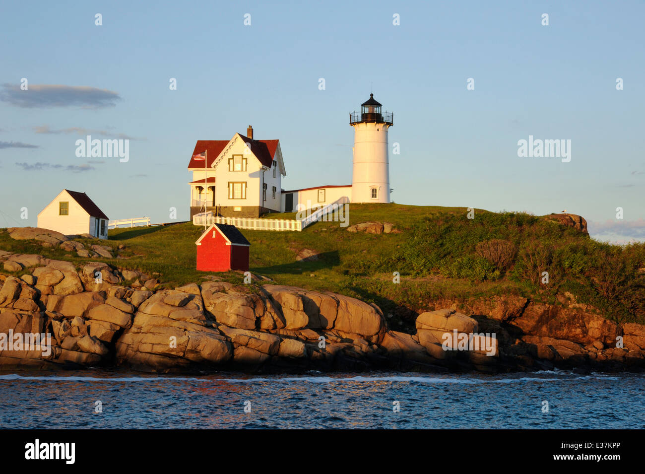 Maine Nubble del faro è illuminato in un caldo colore giallo come il sole tramonta sull'orizzonte di fronte alla luce. Foto Stock