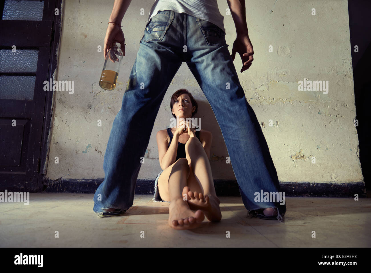 Persone, abuso di sostanze stupefacenti e la violenza domestica. Drunk man standing con bottiglia di whiskey e minacciando la sua giovane moglie a casa Foto Stock