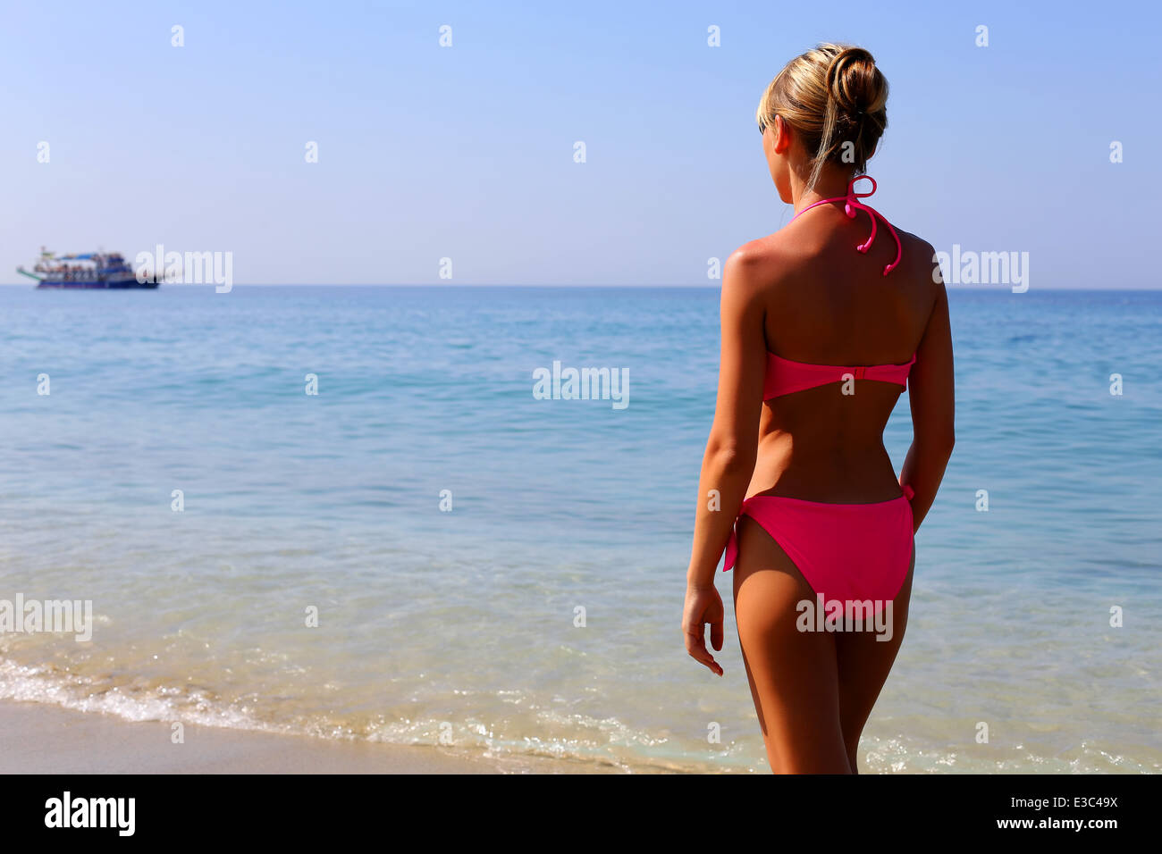 Donna in bikini rosa permanente sulla spiaggia e guardando il mare Foto Stock