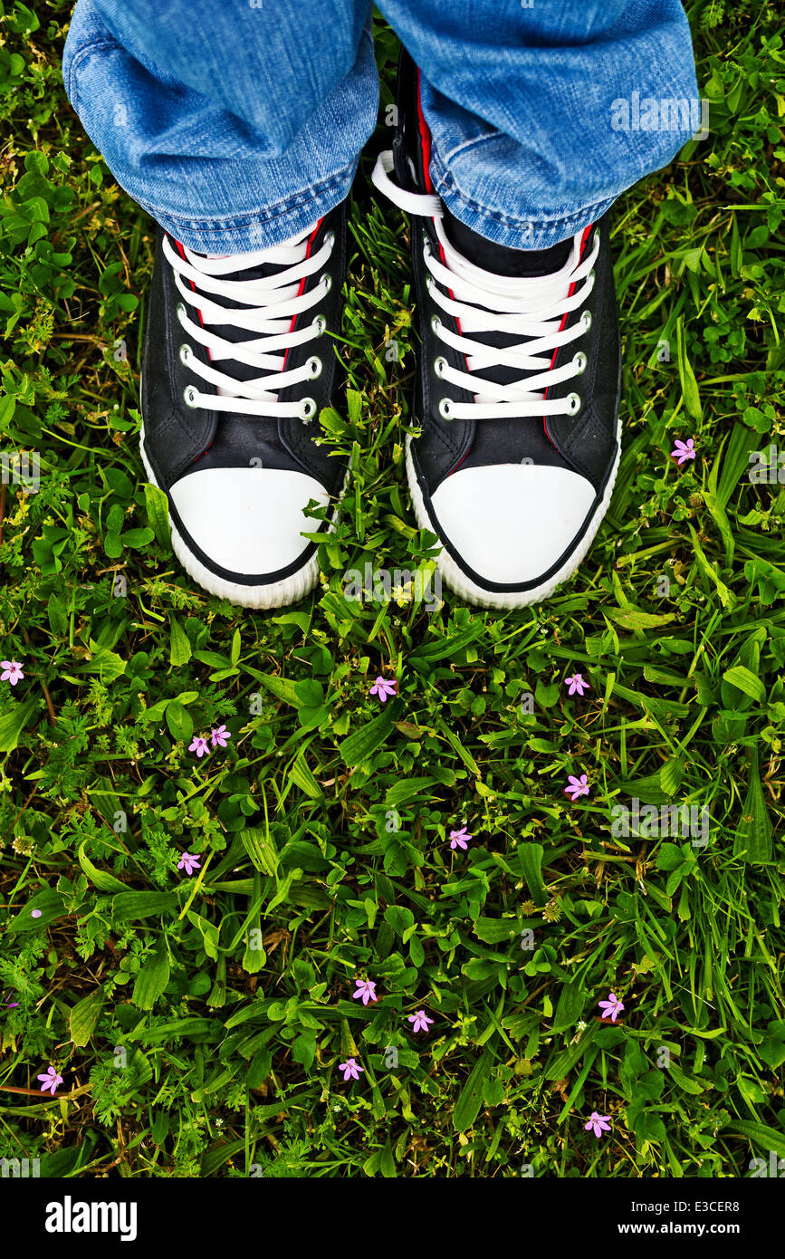 Man in Black sneakers in piedi in fresco verde erba di primavera con fiori. Andando fuori al concetto di natura. Foto Stock