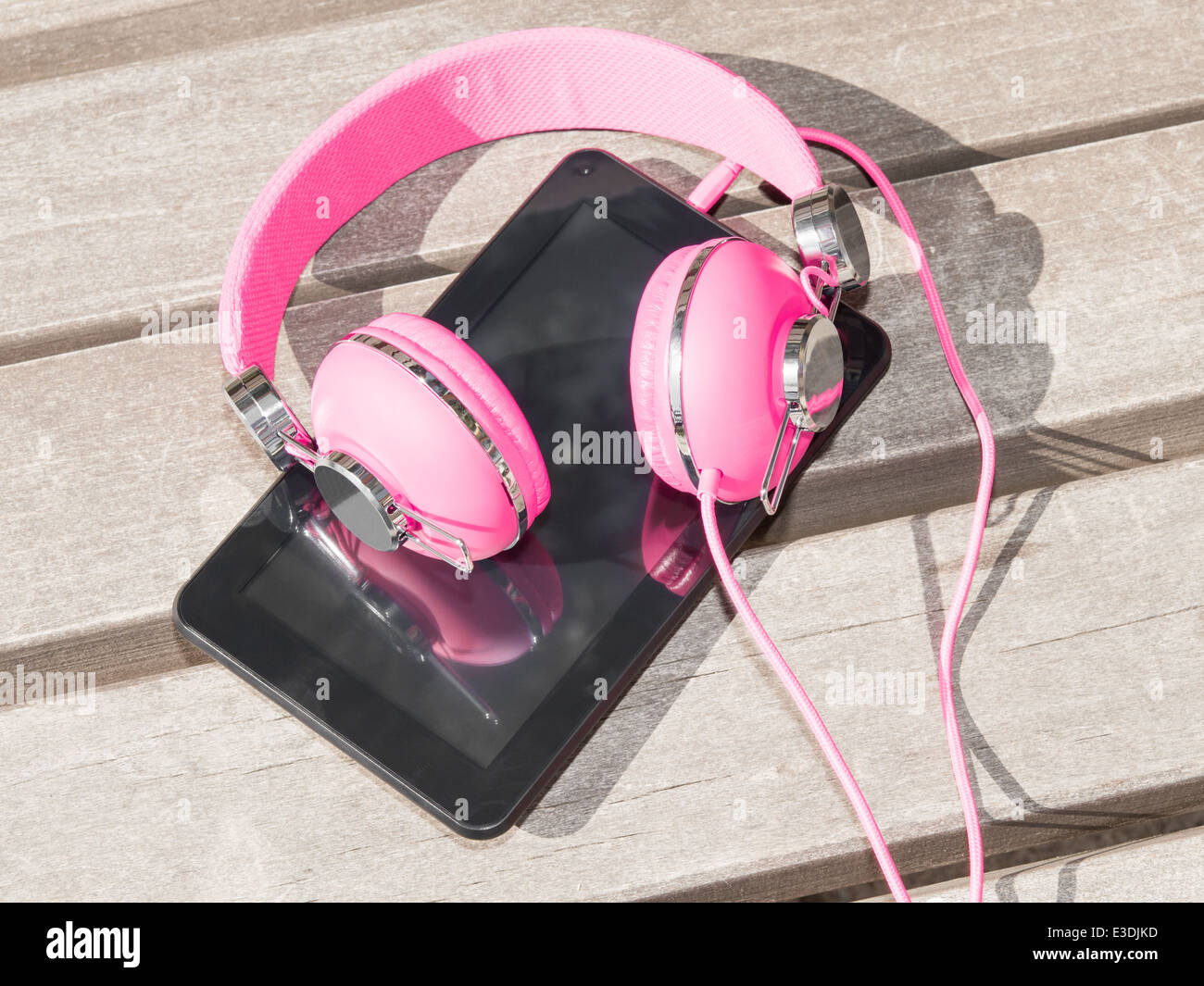 Femmina cuffie rosa e tablet pc per la formazione a distanza e tempo libero mobile all'aperto sul banco di legno in posizione di parcheggio Foto Stock