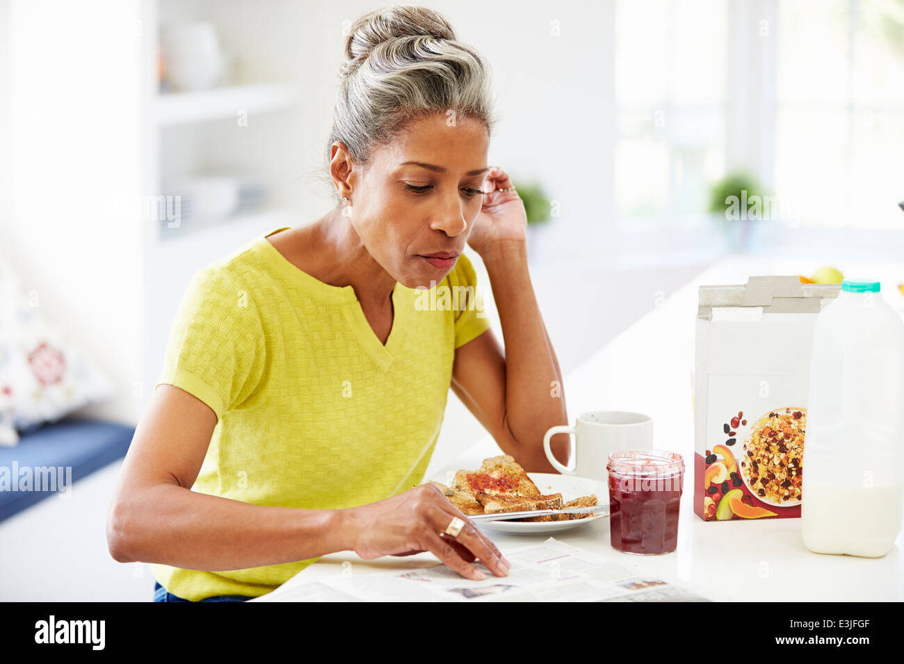 Donna matura di mangiare la prima colazione e il giornale di lettura Foto Stock