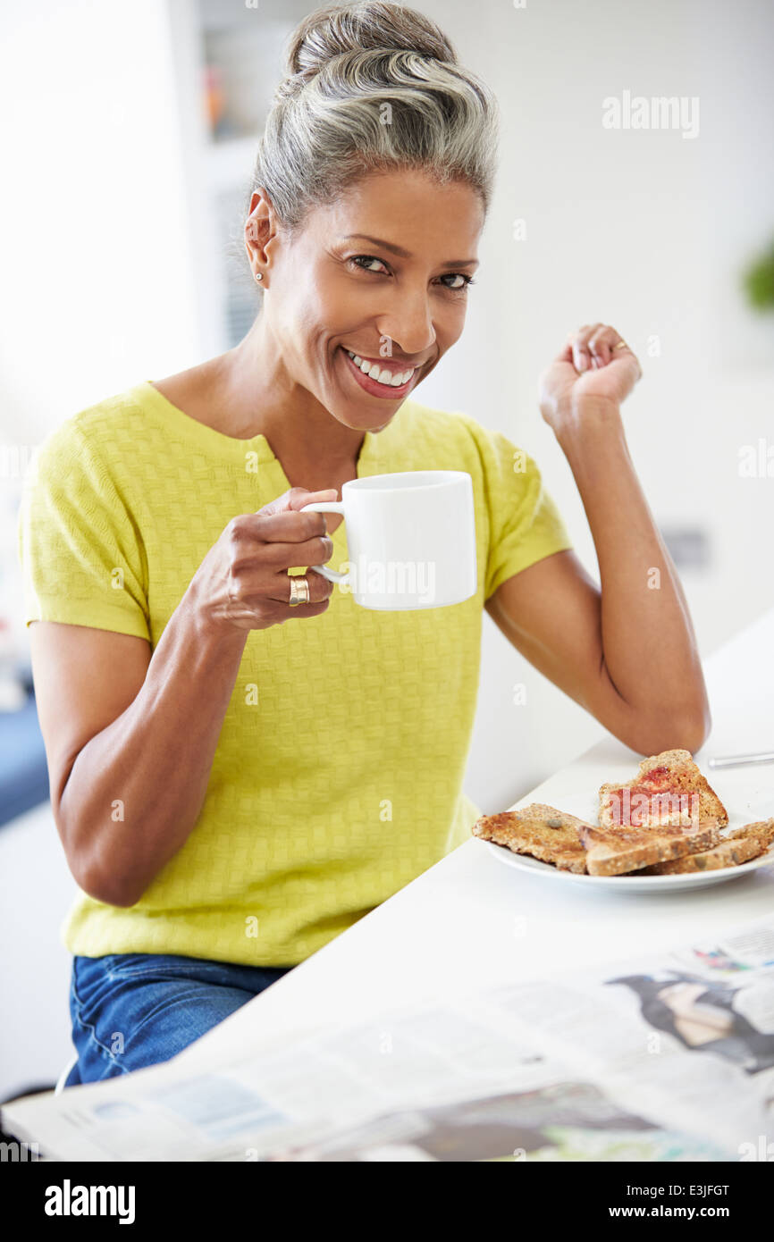 Donna matura di mangiare la prima colazione e il giornale di lettura Foto Stock