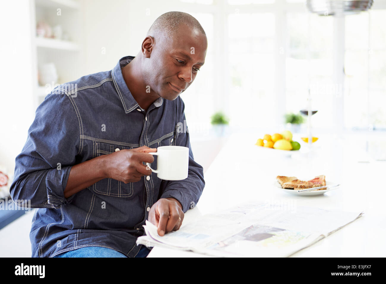 African American uomo mangiare la prima colazione e il giornale di lettura Foto Stock