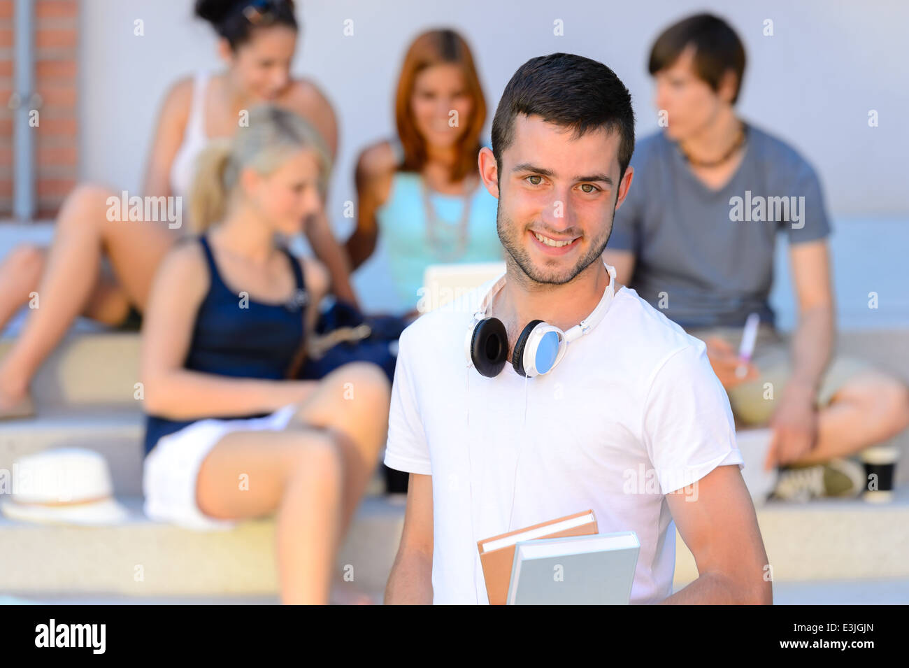 Felice studente ragazzo con libri al di fuori del college amici seduti passi Foto Stock