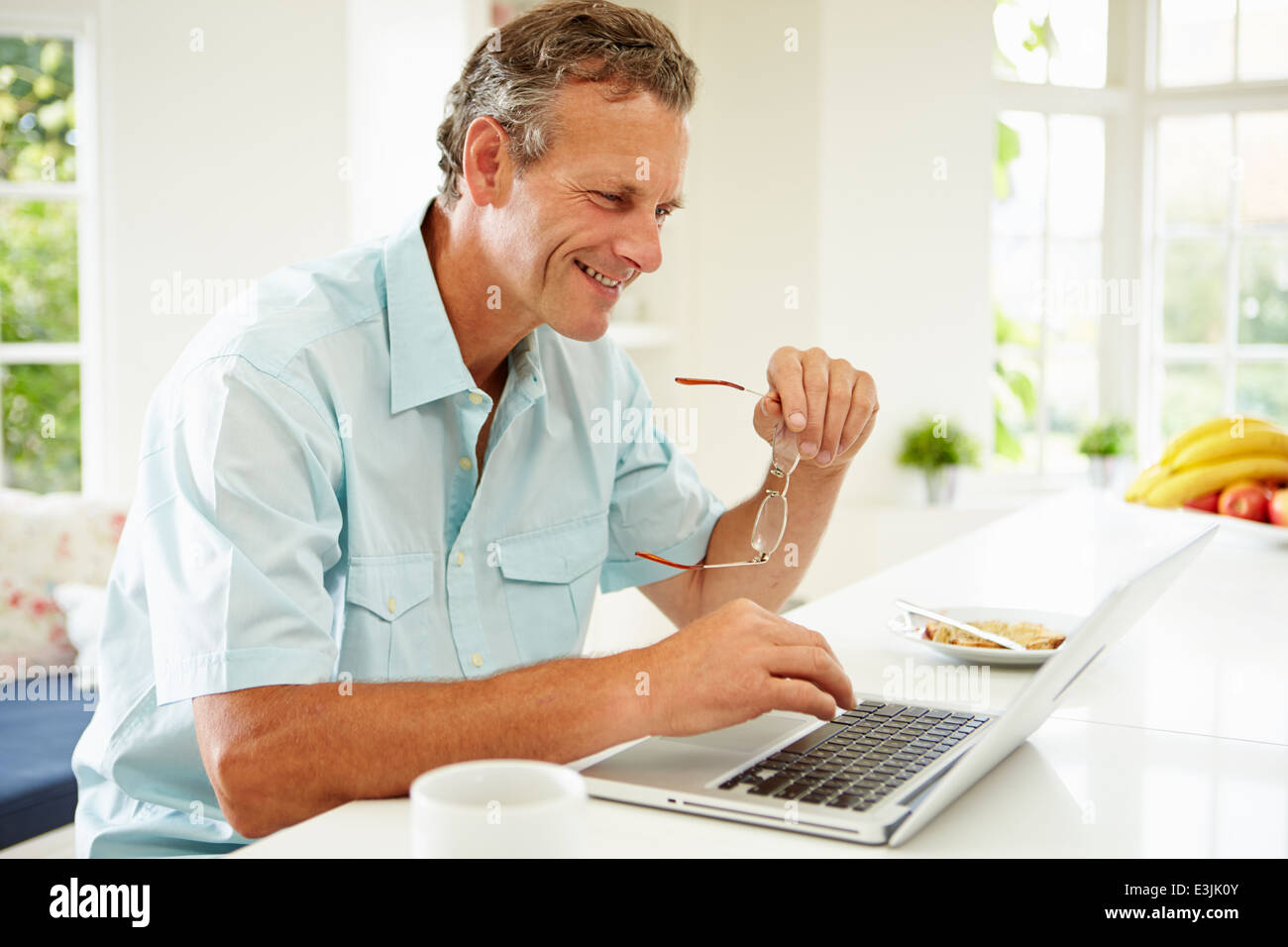 Uomo di mezza età utilizzando laptop tramite la prima colazione Foto Stock