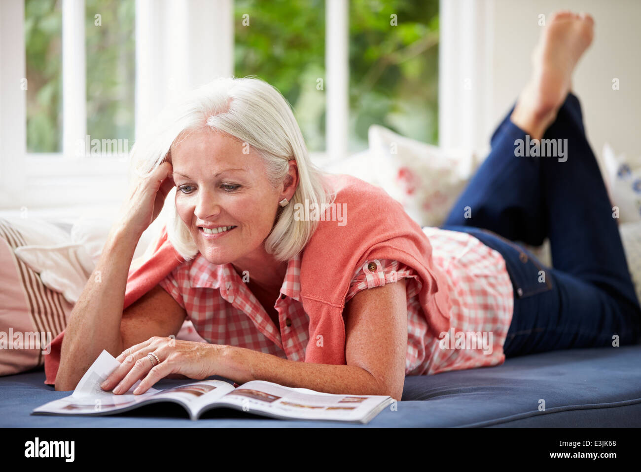 Donna di mezza età rivista lettura sdraiato sul divano Foto Stock