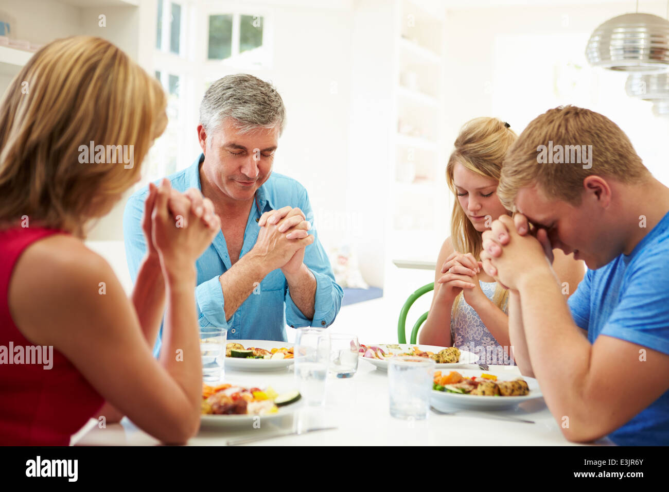 Famiglia dicendo la preghiera prima di mangiare pasti a casa insieme Foto Stock