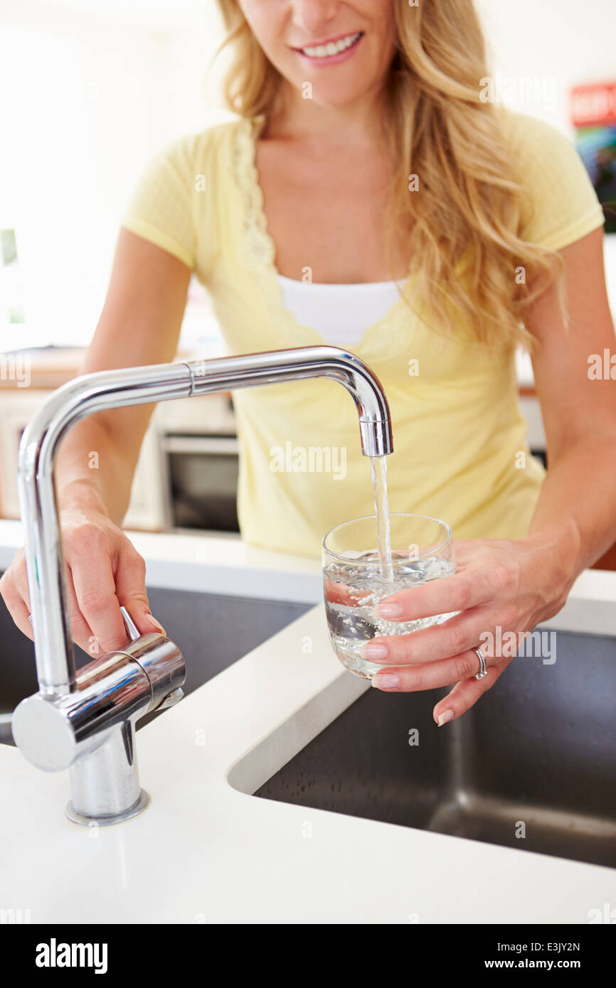 Donna versando un bicchiere di acqua dal rubinetto in cucina Foto Stock