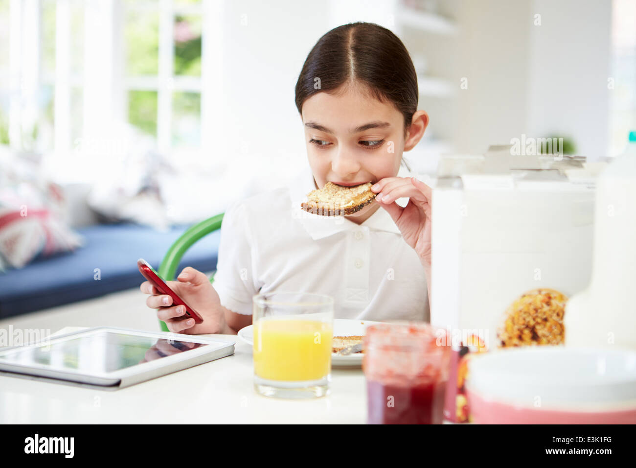 Schoolgirl con tavoletta digitale e mobile di mangiare toast Foto Stock