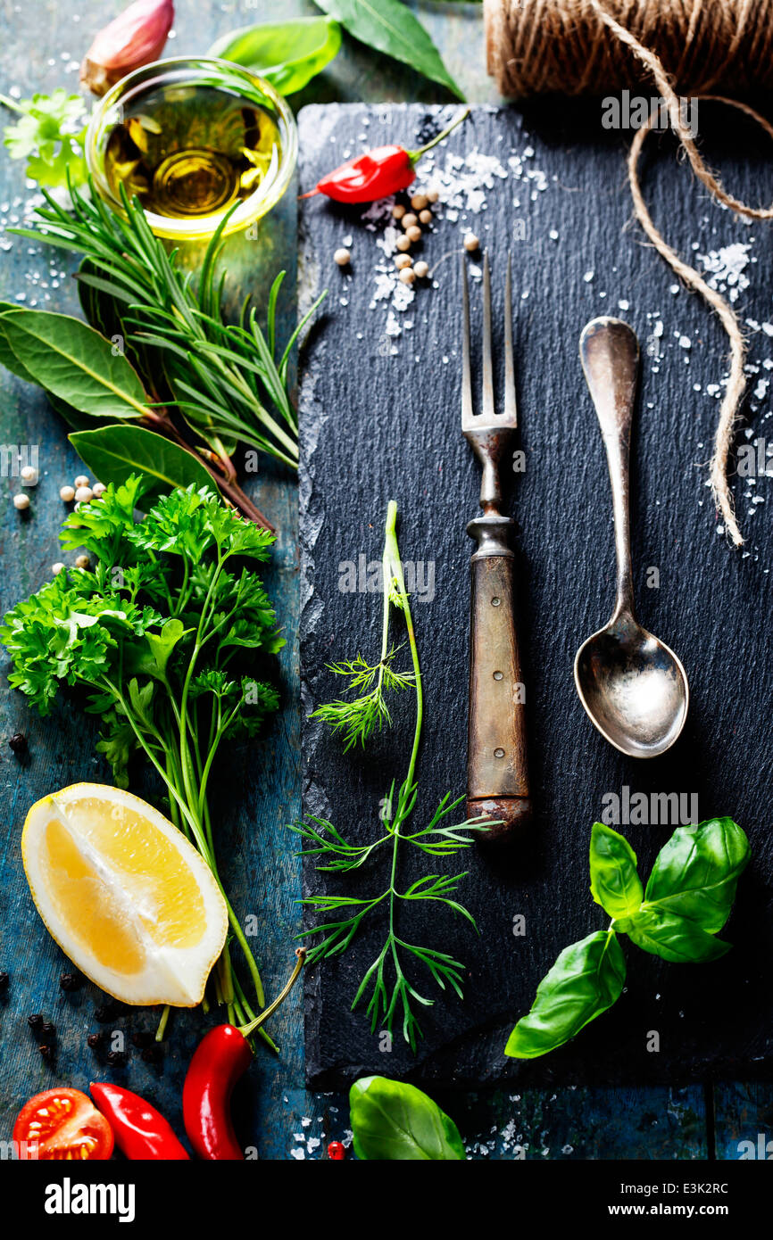 Sfondo di cibo, con erbe aromatiche, spezie, olio d'oliva, sale, i limoni e le verdure. Ardesia e uno sfondo di legno. Foto Stock