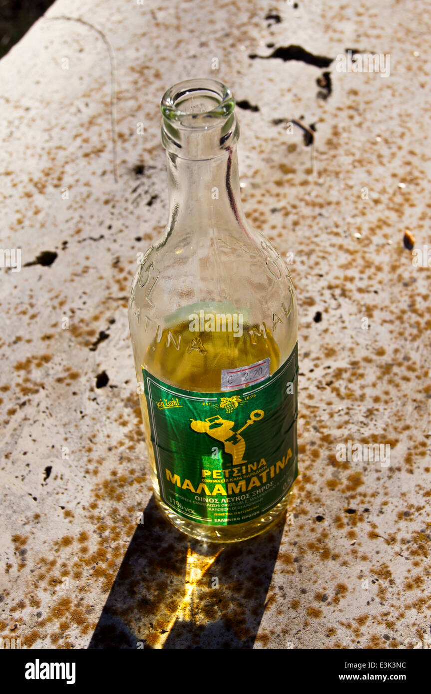 Mezza bottiglia piena di retsina vino bianco in silhouette su una panchina nel parco, Kos, Grecia Foto Stock