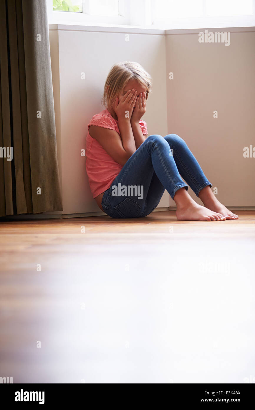 Infelice bambino seduto sul pavimento in un angolo a casa Foto Stock