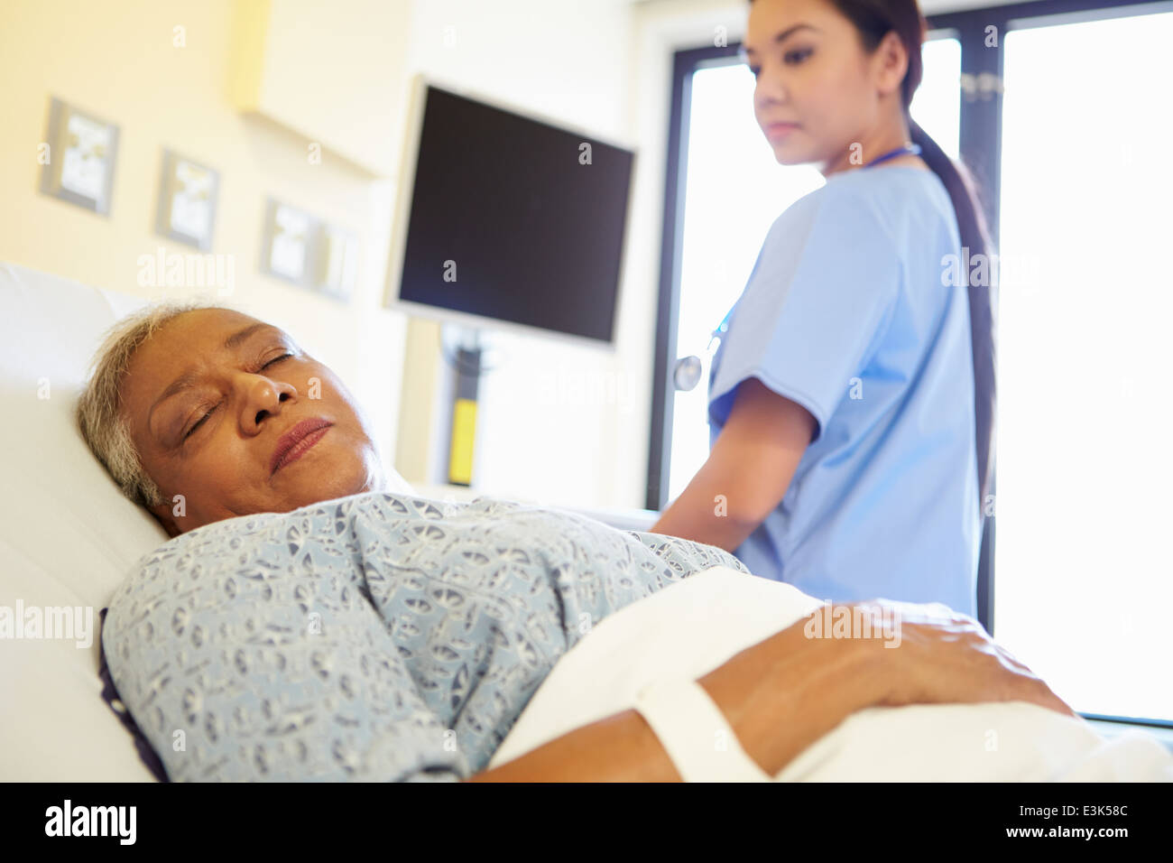 L'infermiera guardando Sleeping Senior donna paziente in ospedale Foto Stock