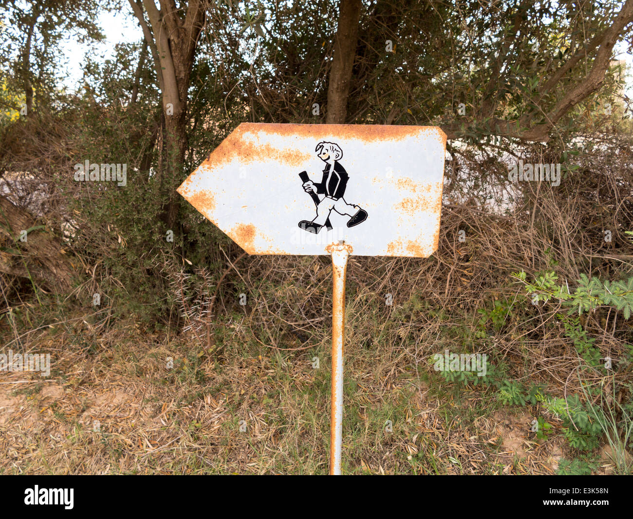 Un arrugginendo metallo sentiero segno rivolta a sinistra mostra una illustrazione di un sorridente uomo a piedi con bastone Foto Stock