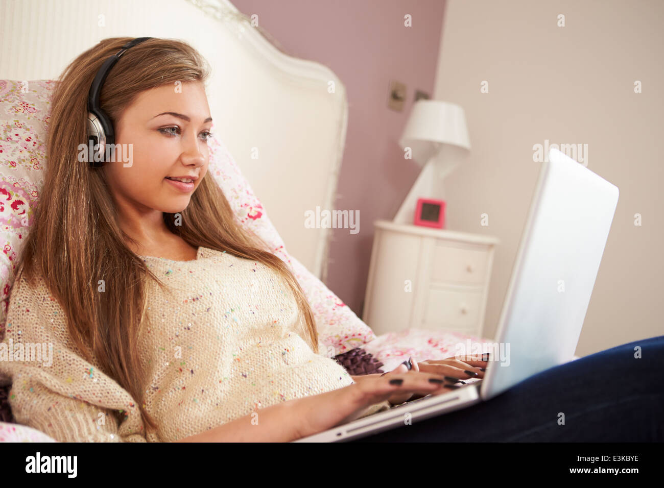 Ragazza adolescente sdraiato sul letto tramite computer portatile che indossano le cuffie Foto Stock