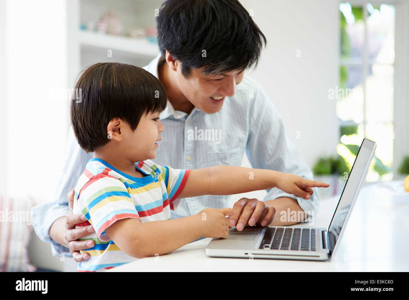 Asian Padre aiutando figlio per uso portatile a casa Foto Stock