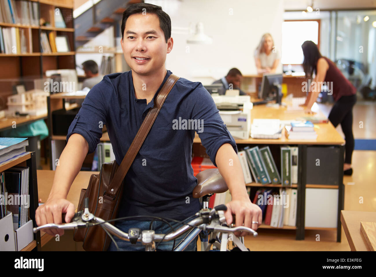 Architetto arriva a lavorare sulla moto spingendolo attraverso Office Foto Stock