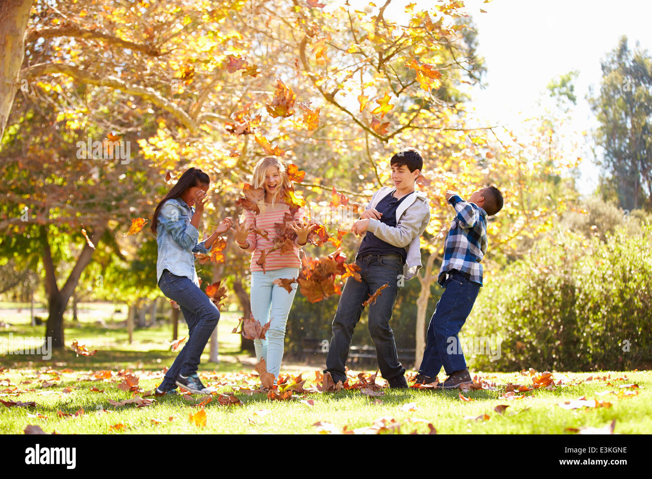 Quattro bambini gettando le foglie di autunno in aria Foto Stock
