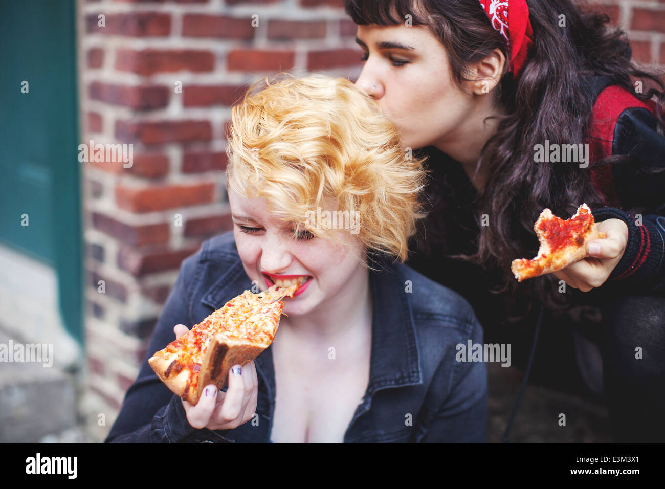 Giovane donna baciare il suo amico mentre mangiare la pizza Foto Stock