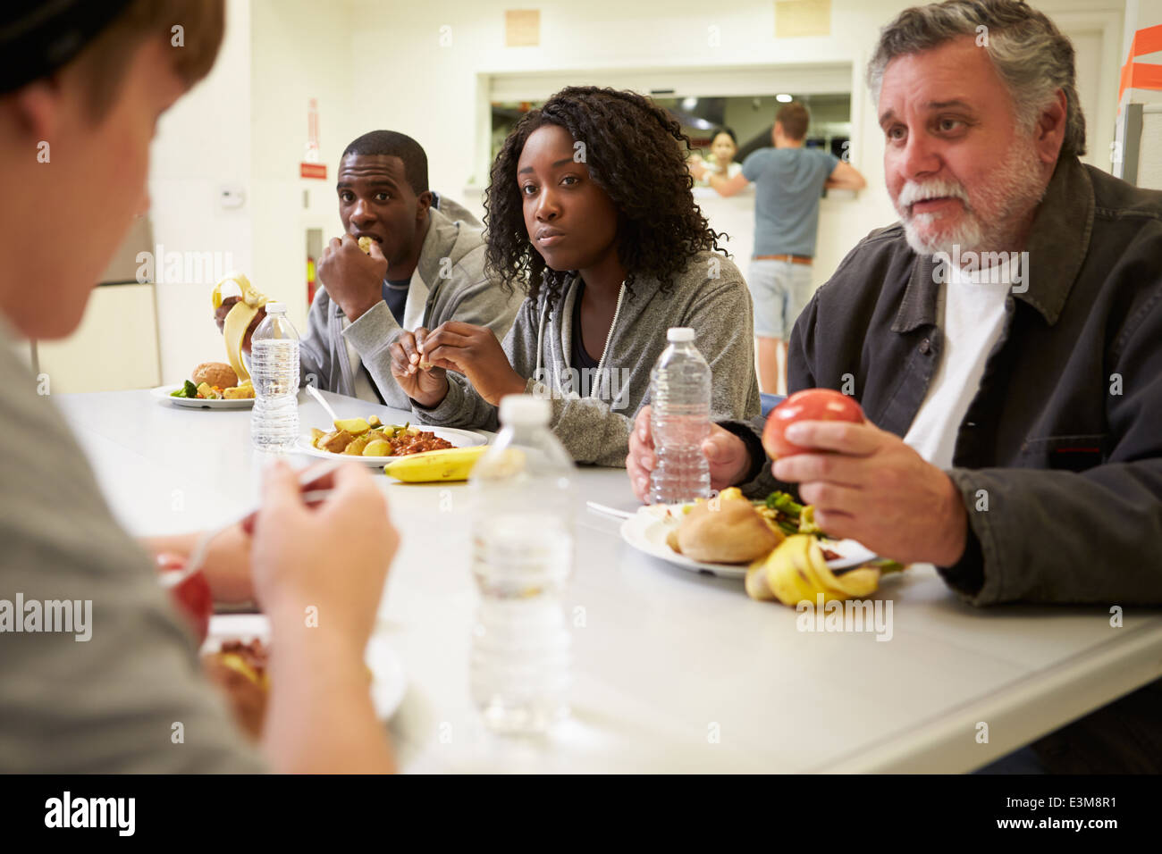 La gente seduta a tavola a mangiare cibo in rifugio senzatetto Foto Stock