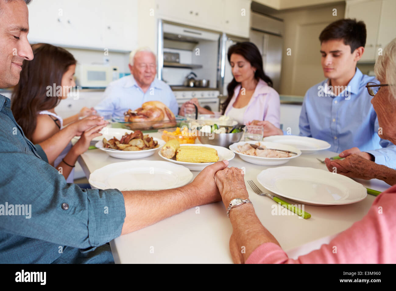 Famiglia Multi-Generation dicendo la preghiera prima di mangiare pasti Foto Stock