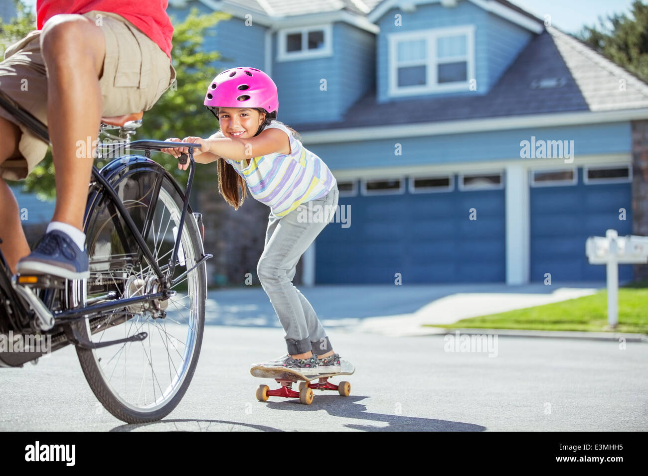 Padre sulla bicicletta la figlia di tiro su skateboard Foto Stock