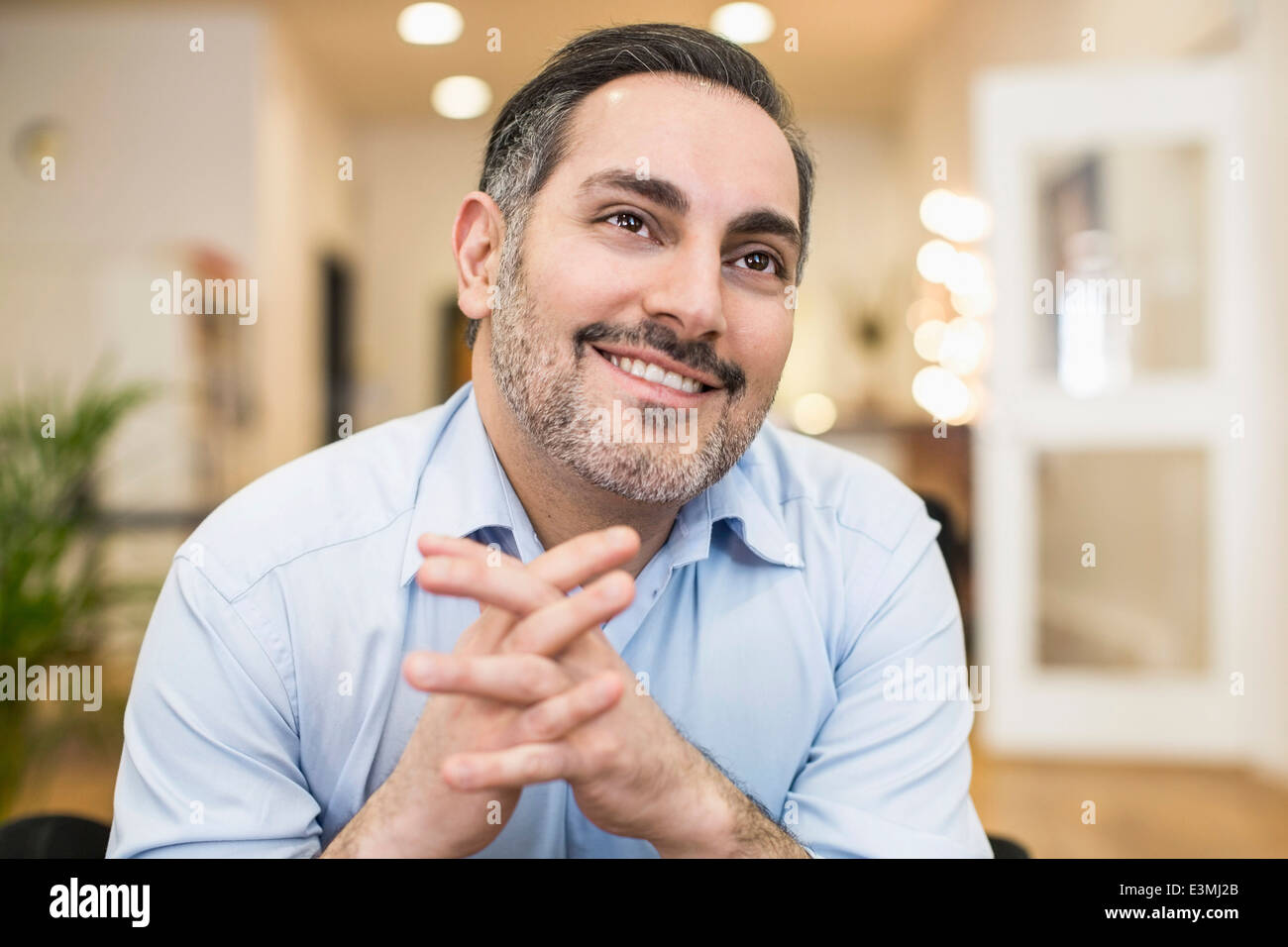 Imprenditore sorridente con le mani incrociate che guarda lontano in office Foto Stock