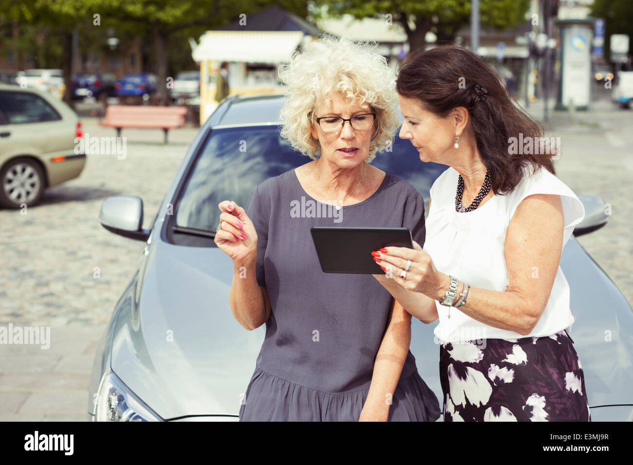 Femmina Senior amici utilizzando la tavoletta digitale contro l'auto sulla strada Foto Stock