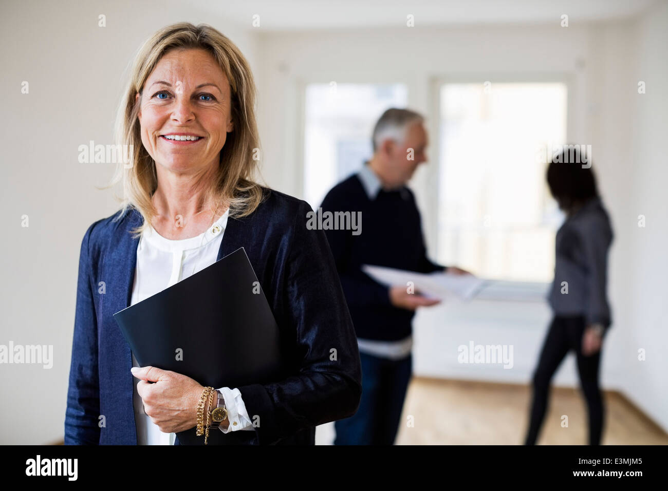 Ritratto di fiducioso agente immobiliare con un collega e la donna in background a casa Foto Stock