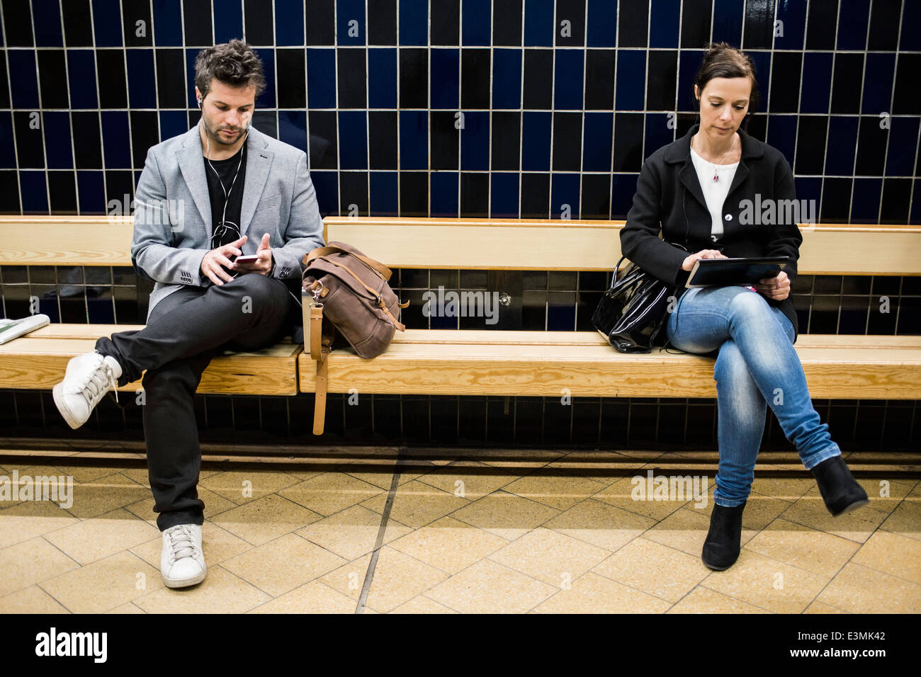 A lunghezza piena di persone che utilizzano tecnologie sulla panchina alla stazione della metropolitana Foto Stock