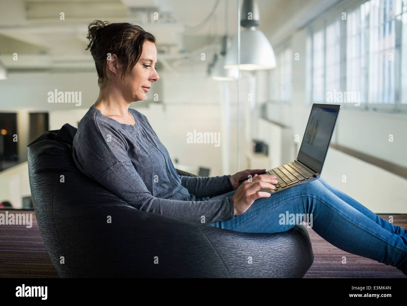 Vista laterale della coppia imprenditrice utilizzando computer portatile mentre è seduto sul bean bag in office Foto Stock