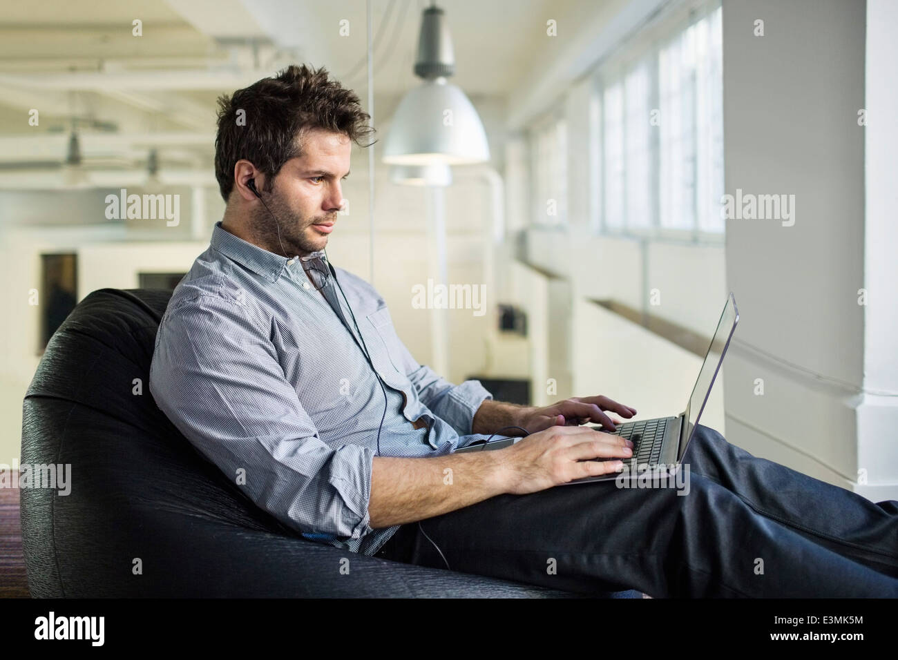 Metà adulto uomo d affari con computer portatile mentre è seduto sul bean bag in office Foto Stock