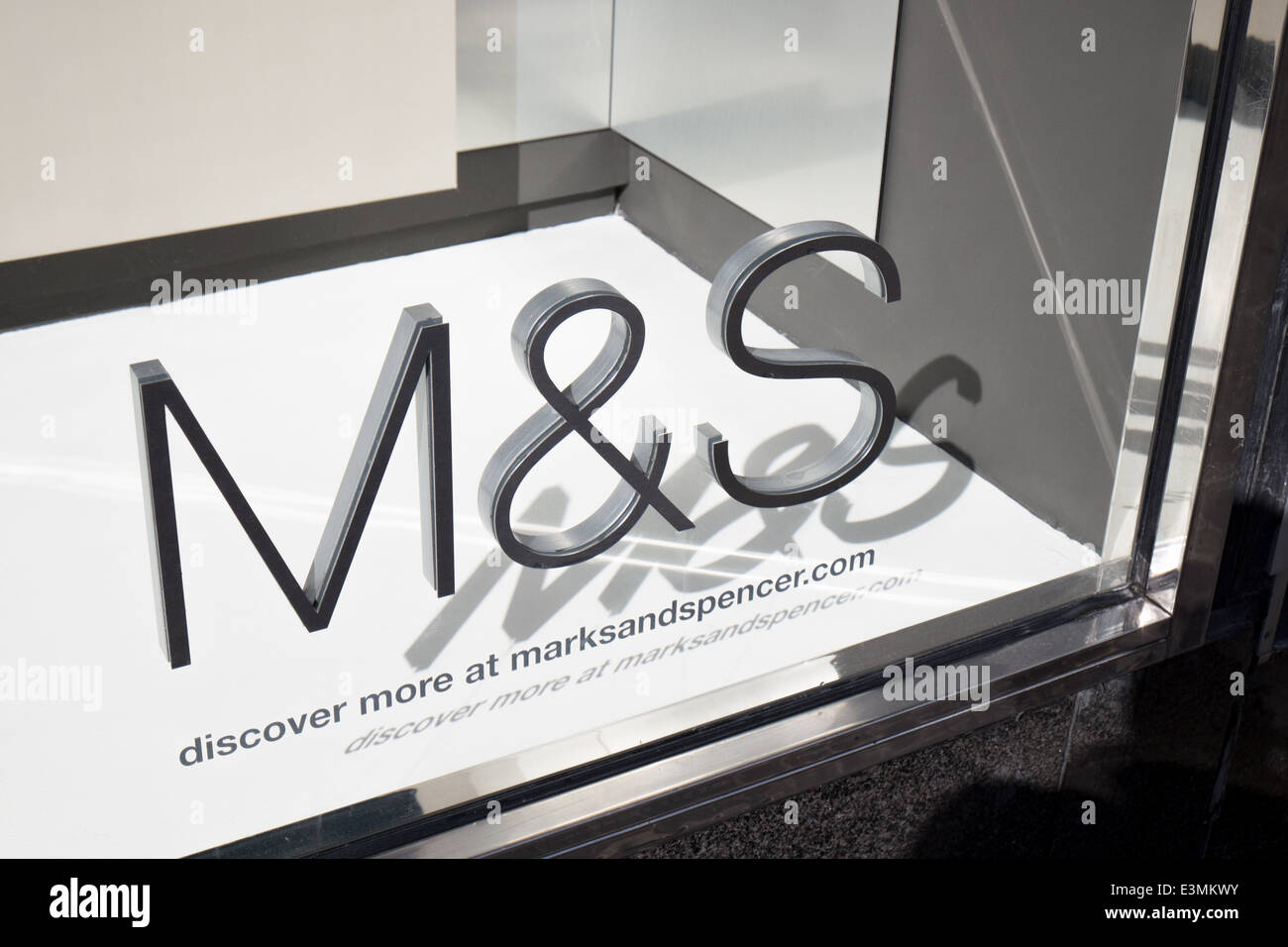 Sole brillante sul Marks & Spencer logo aziendale su un negozio di vetro fusione anteriore un'ombra nelle vetrine area di visualizzazione Foto Stock