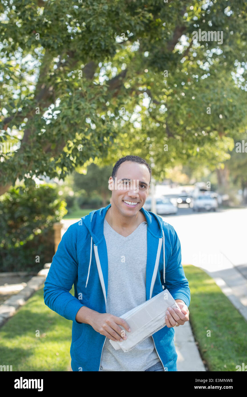 Ritratto di uomo sorridente con il giornale sul marciapiede Foto Stock