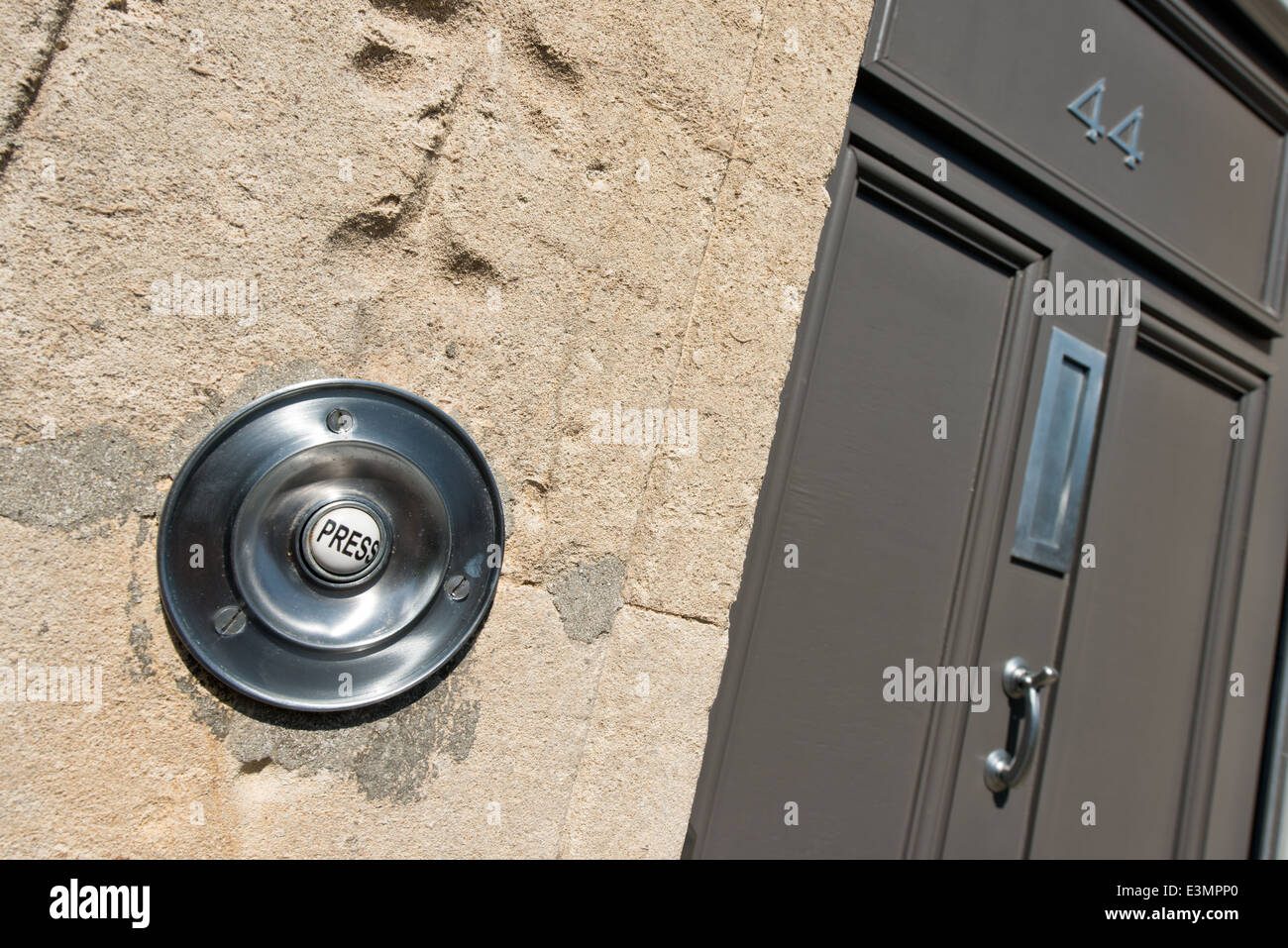 Una circolare cromato campanello della porta su un bagno a spiovente muro di pietra con la parola premere sul pulsante con una porta anteriore Foto Stock