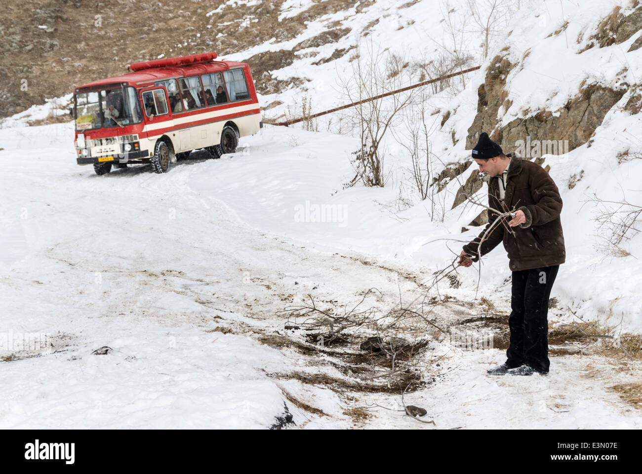 Impostazione uomo rami sulla strada per aiutare un autobus che passa al di sopra di una patch scivoloso sulla strada, Armenia Foto Stock