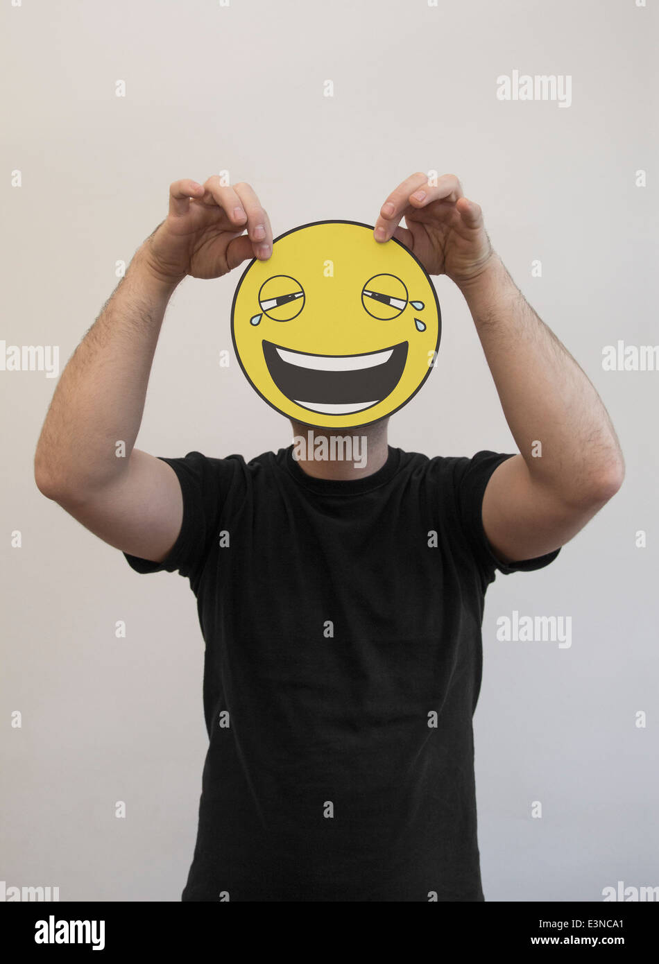 L'uomo tenendo un ridere e piangere emoticon nella faccia anteriore del suo volto Foto Stock