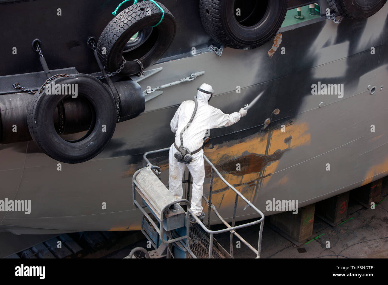 Uomo di verniciatura a spruzzo di cofano nave grigio nel dock Foto Stock