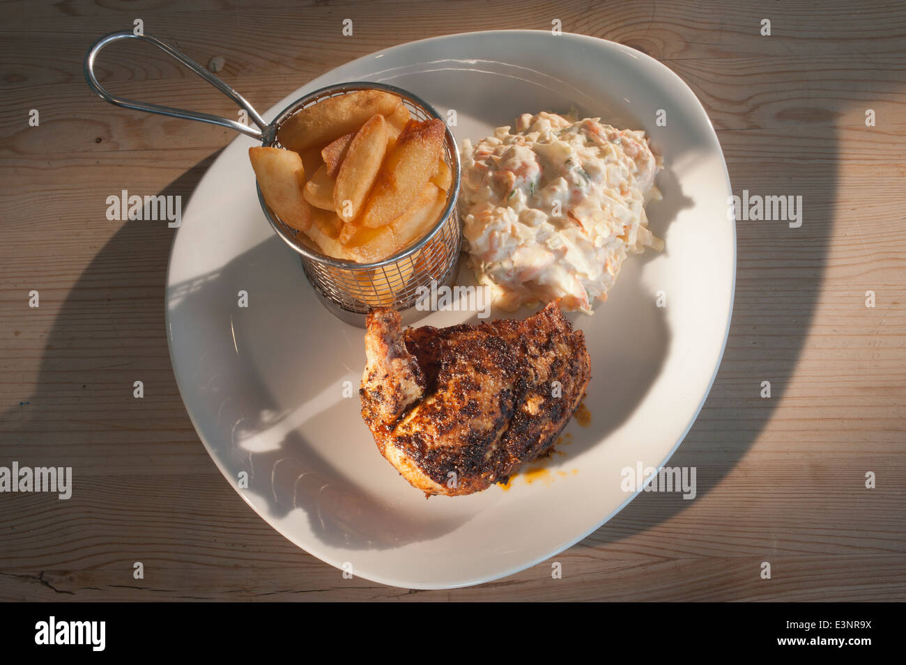 Coscia di pollo arrosto con spezie asiatiche servita con coleslaw e patatine o patate fritte su una piastra bianca e un tavolo di legno. Foto Stock