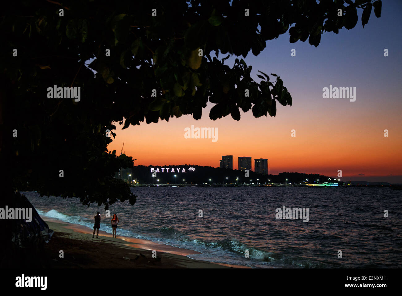 I turisti sulla spiaggia durante il tramonto con il Pattaya insegna al neon in background in Pattaya, Thailandia Foto Stock