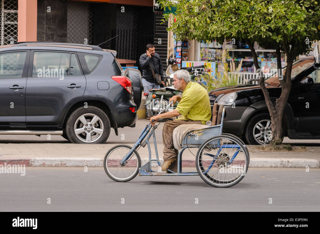 Un uomo utilizza mano-pedali a pedale un triciclo lungo una strada a Marrakech, Marocco Foto Stock