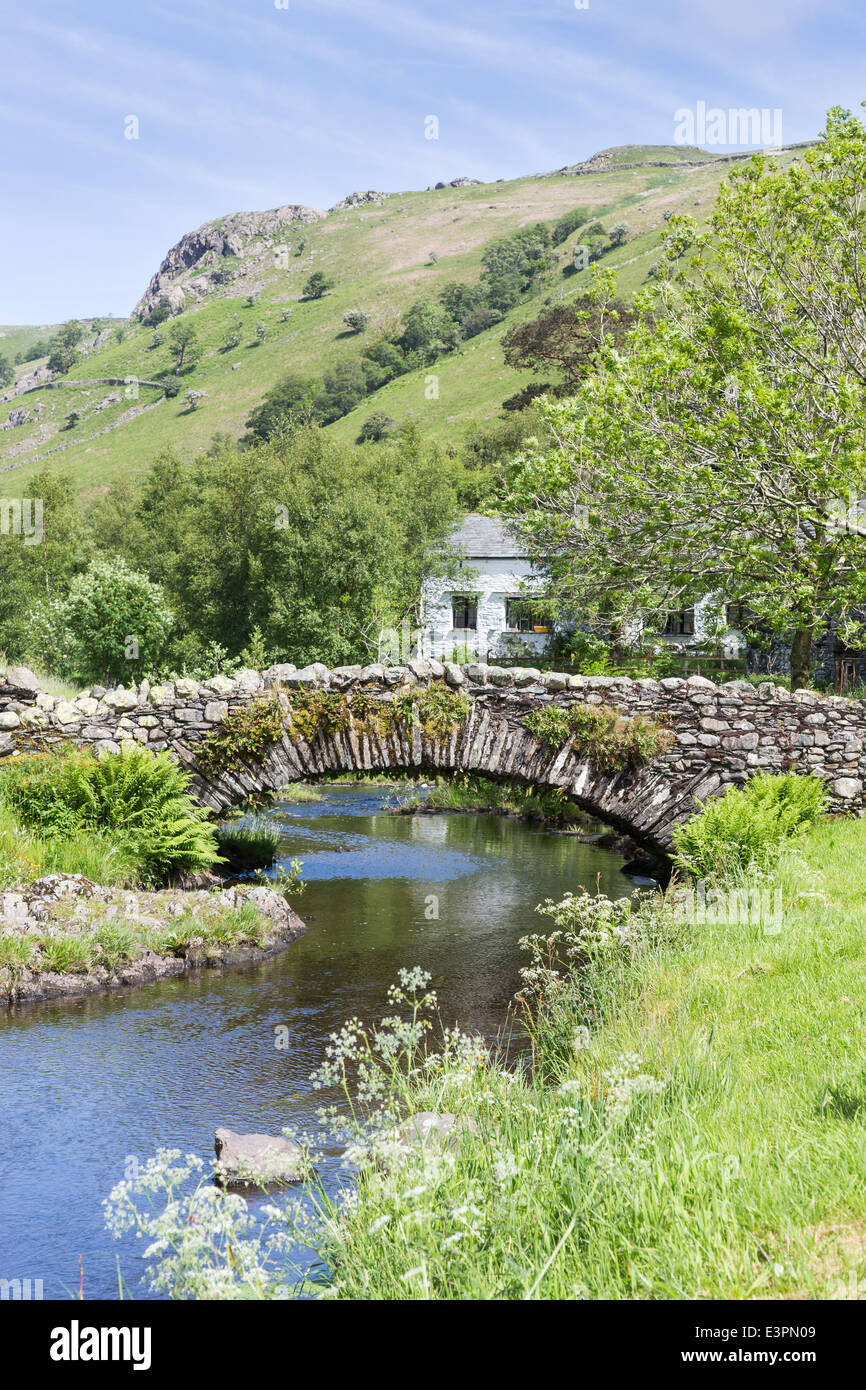 Stalattite tradizionale costruito Packhorse Bridge a Watendlath, Borrowdale, Lake District con abbastanza imbiancato cottage in pietra Foto Stock